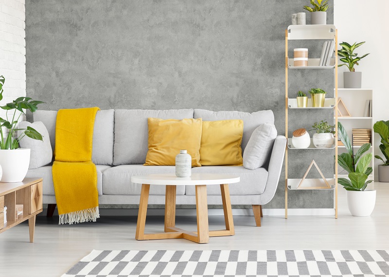 Yellow pillows and blanket on grey sofa in modern living room interior with plants and carpet. Real photo Πλαστική επένδυση Ραμποτέ PVC VILO Concrete Stone 25x265 cm - Image 3